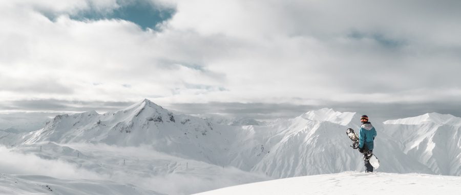 snowboarder at the top of a mountain looking at the snow capped mountains in the distance