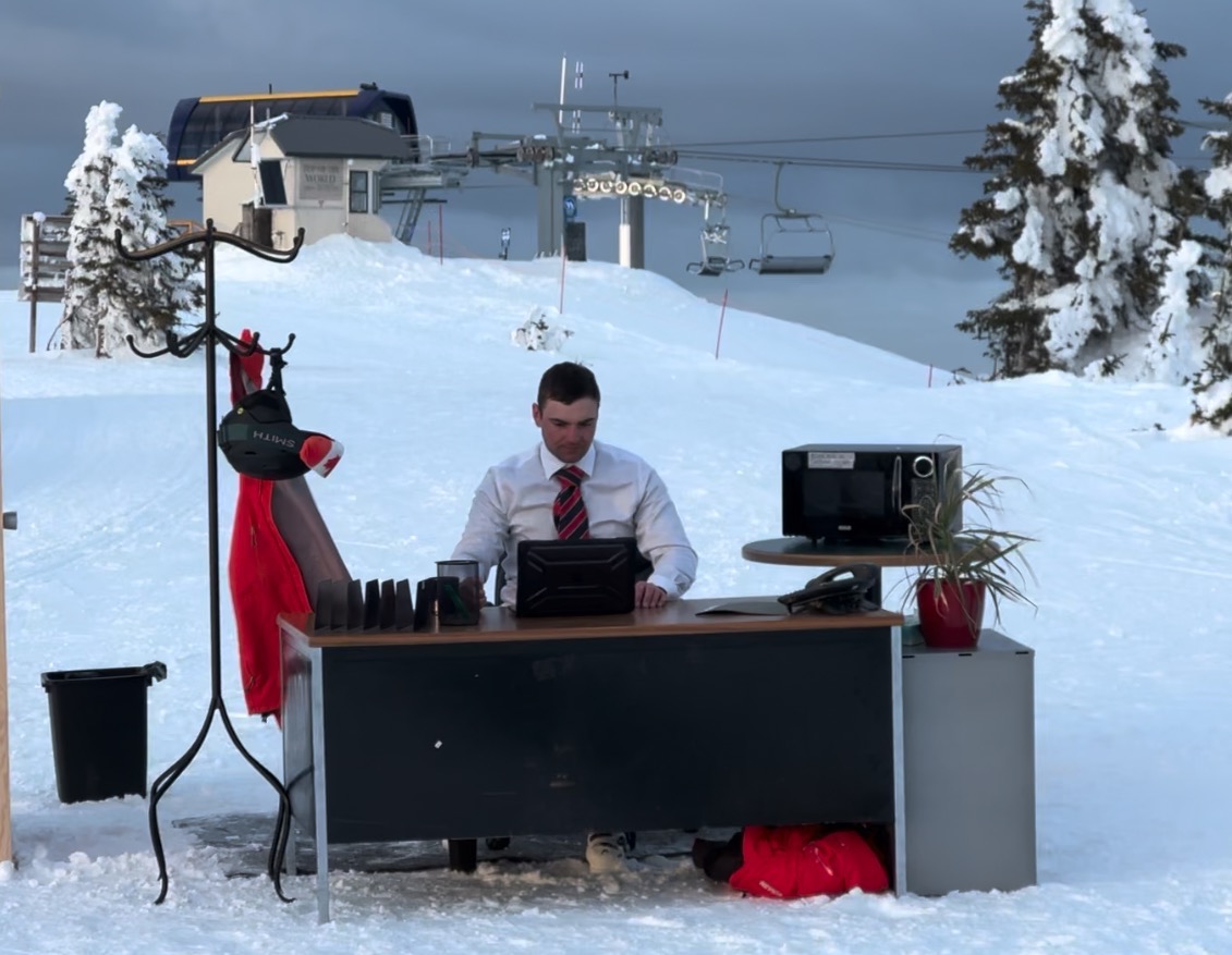 man sat at desk in an office scene on top of ski resort mountain